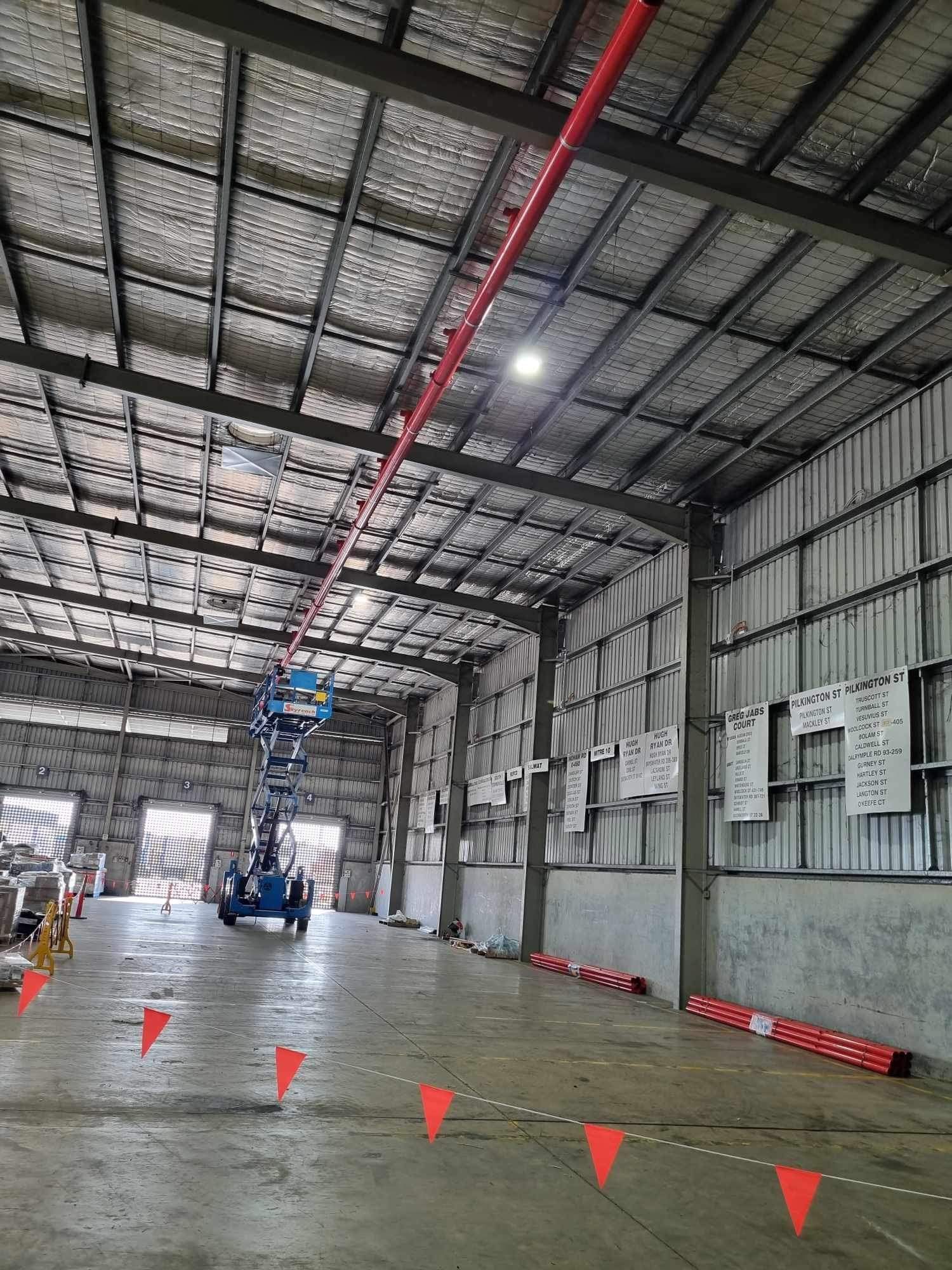 Empty Warehouse Interior With a Worker Lift, Red Floor Cones, and a Reflective Polished Concrete Floor — Flaming North Fire Protection Pty Ltd in Garbutt, QLD