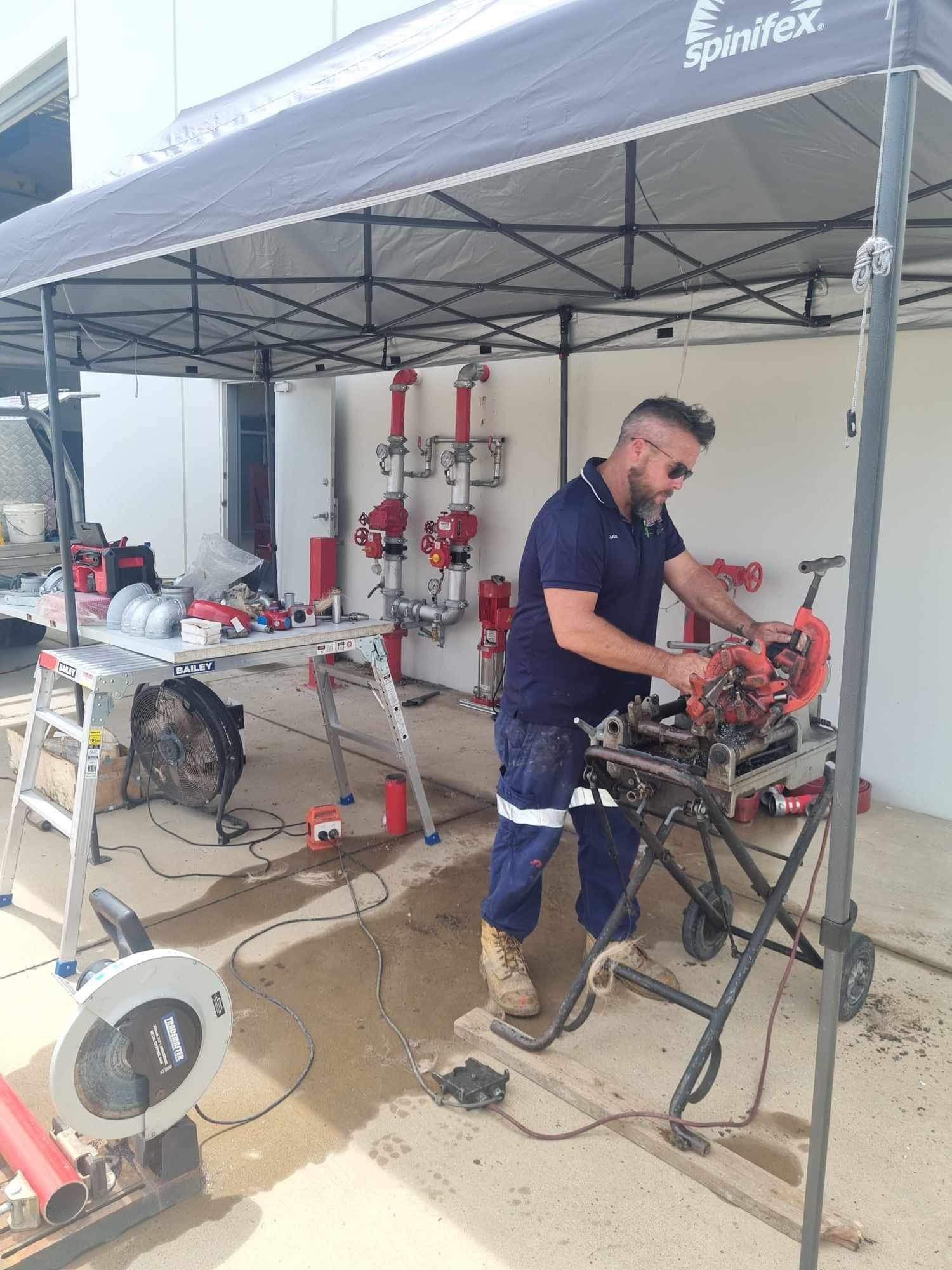 Mechanic Repairing an Engine Under a Canopy in a Workshop Area With Tools and Equipment Nearby — Flaming North Fire Protection Pty Ltd in Garbutt, QLD