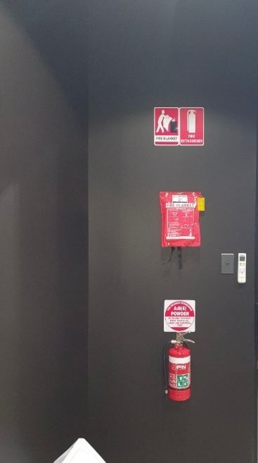 Black Wall With Red Fire Safety Signs and a Fire Extinguisher Mounted Below — Flaming North Fire Protection Pty Ltd in Cairns, QLD