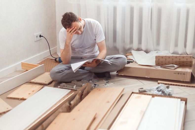 Person sitting on the floor, holding their head amid scattered wooden boards during home renovation
