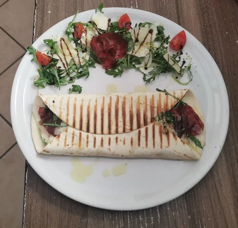 Piadina grigliata servita su un piatto con una piccola insalata di contorno e fragole su un tavolo di legno.