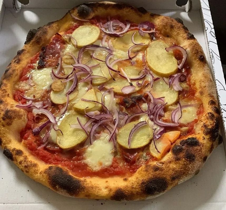 Pizza condita con fette di cipolla rossa e rondelle di patate in una scatola aperta