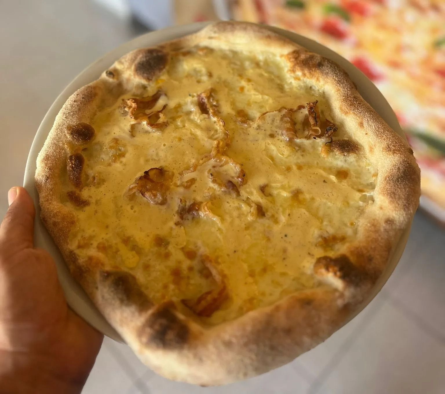 Pizza rotonda da mangiare con le mani, con crosta dorata e formaggio, ripresa ravvicinata in un ambiente di cucina.