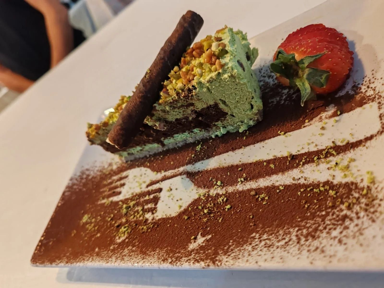 Dessert impiattato con gelato al gusto di menta, cialda al cioccolato, fragola e una spruzzata di cacao in polvere.