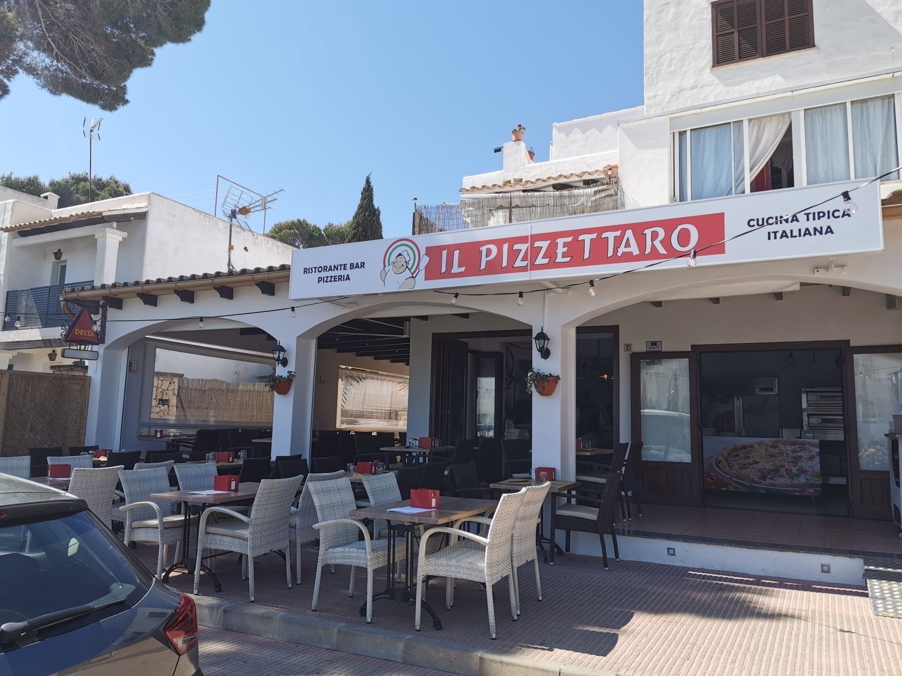 Vista esterna del ristorante Il Pizzattaro con tavoli e sedie da patio sotto una tenda bianca.