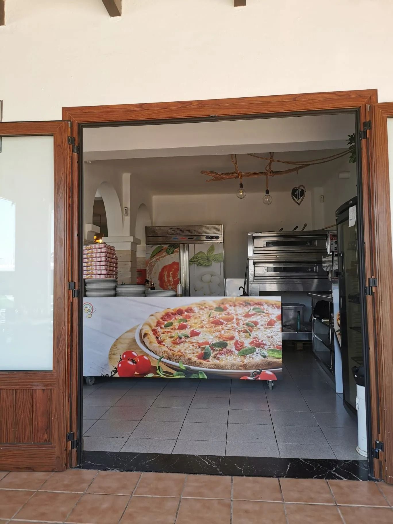 Locale aperto con bancone per alimenti, poster della pizza, pavimento piastrellato e attrezzature da cucina all'interno.
