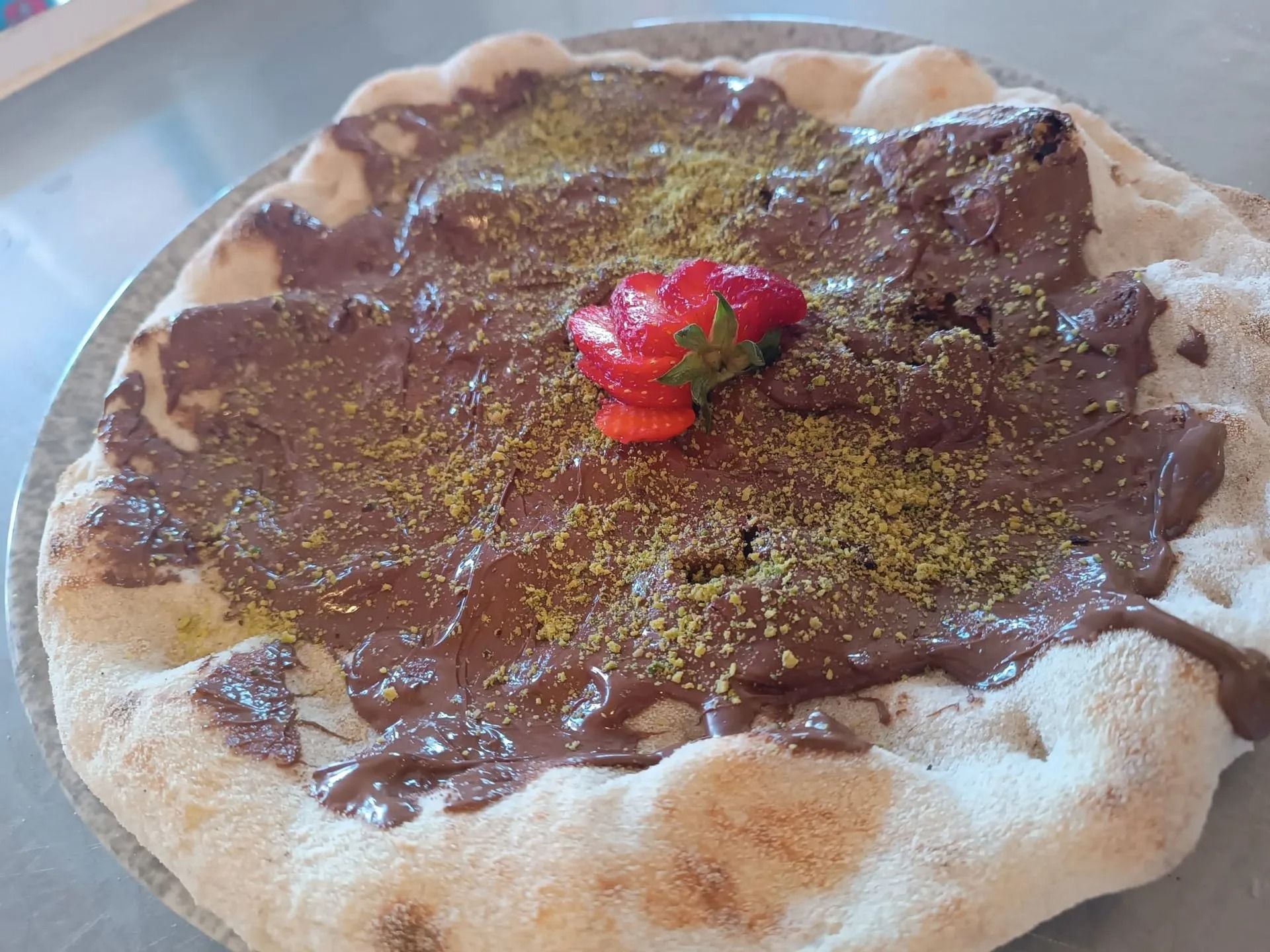 Torta al cioccolato con granella di pistacchio e guarnizione di fragole, servita su un piatto.