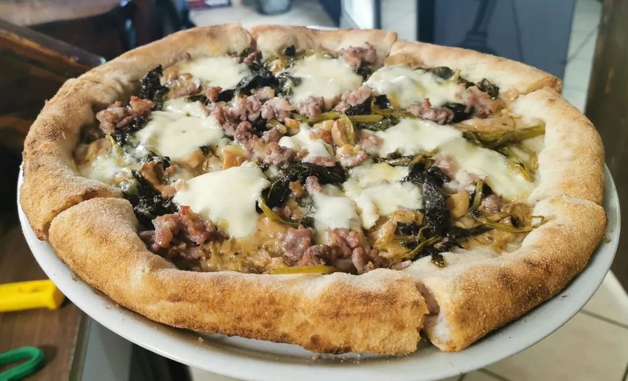 Pizza con formaggio fuso e crosta spessa, servita su un vassoio di metallo, con carne tritata e verdure.
