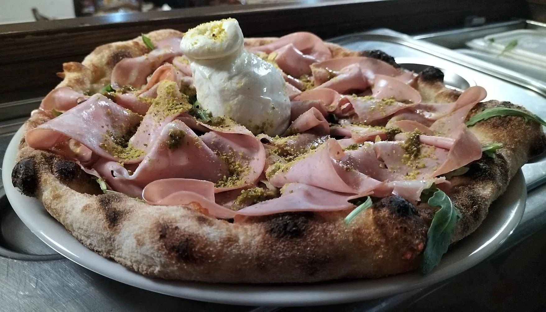 Pizza con prosciutto cotto ripiegato, uovo in camicia ed erbe aromatiche su un vassoio di metallo