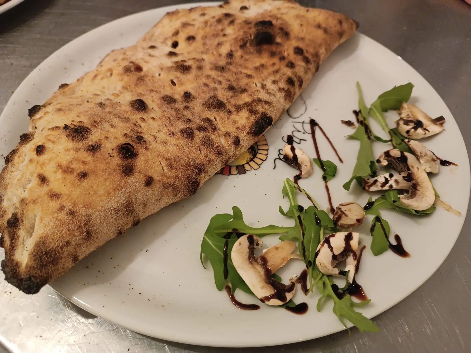 Calzone su un piatto con una piccola insalata di rucola e un filo di aceto balsamico.