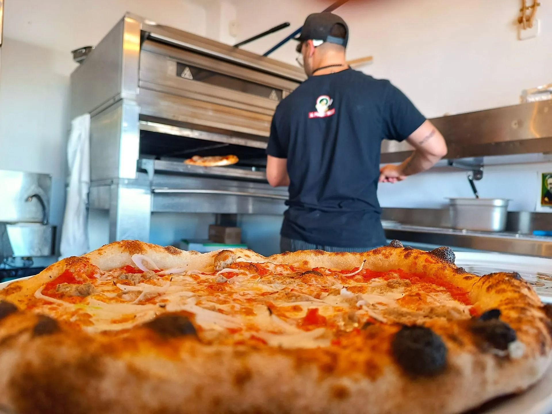 Forno per pizza con un operaio in camicia nera che prepara una pizza in cucina
