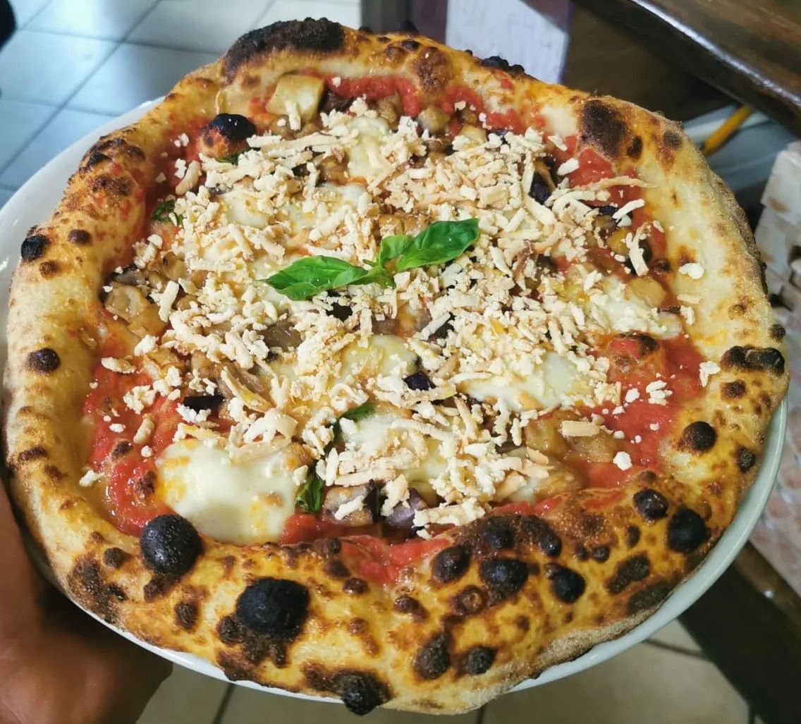 Primo piano di una pizza con salsa di pomodoro, formaggio fuso, basilico e crosta bruciacchiata su un piatto.