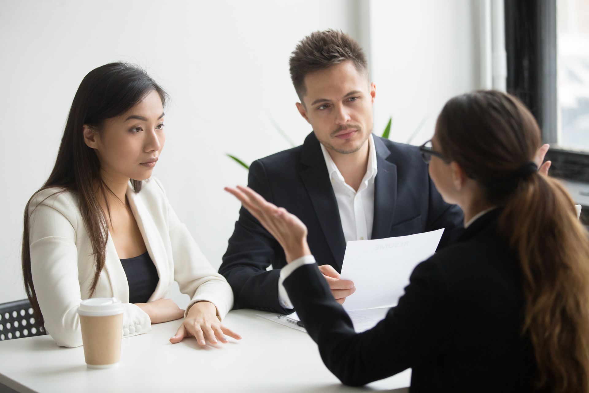 Woman explaining something to a couple at a table, gesturing with her hands; office setting.