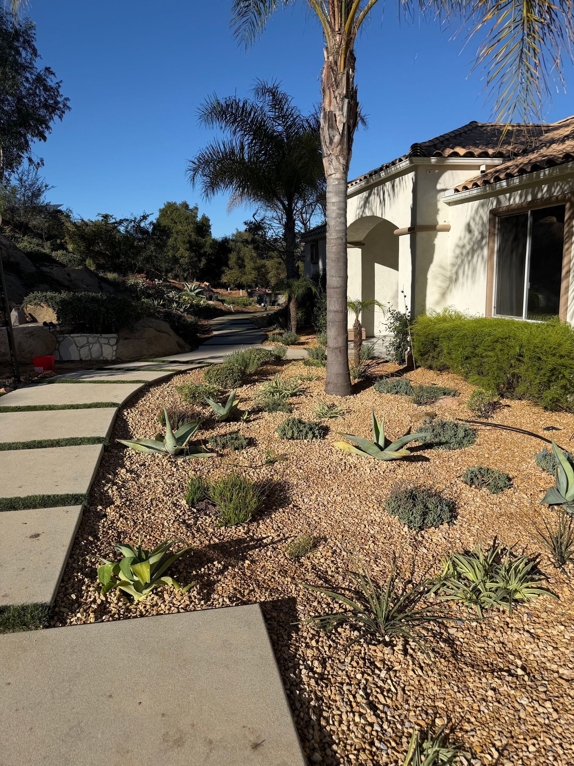 Front yard with stepping stones, mulch bed, and a house under a clear blue sky