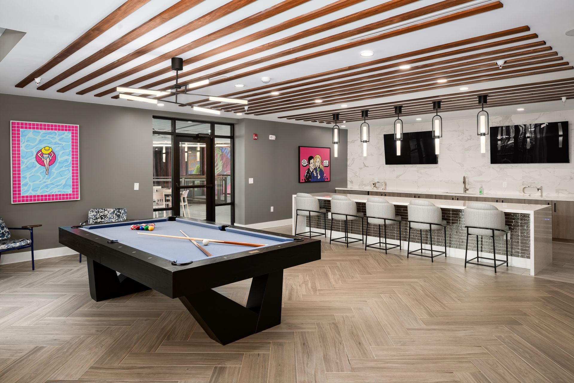Modern lounge with a pool table, bar seating, chevron wood flooring, and slatted wood ceiling.