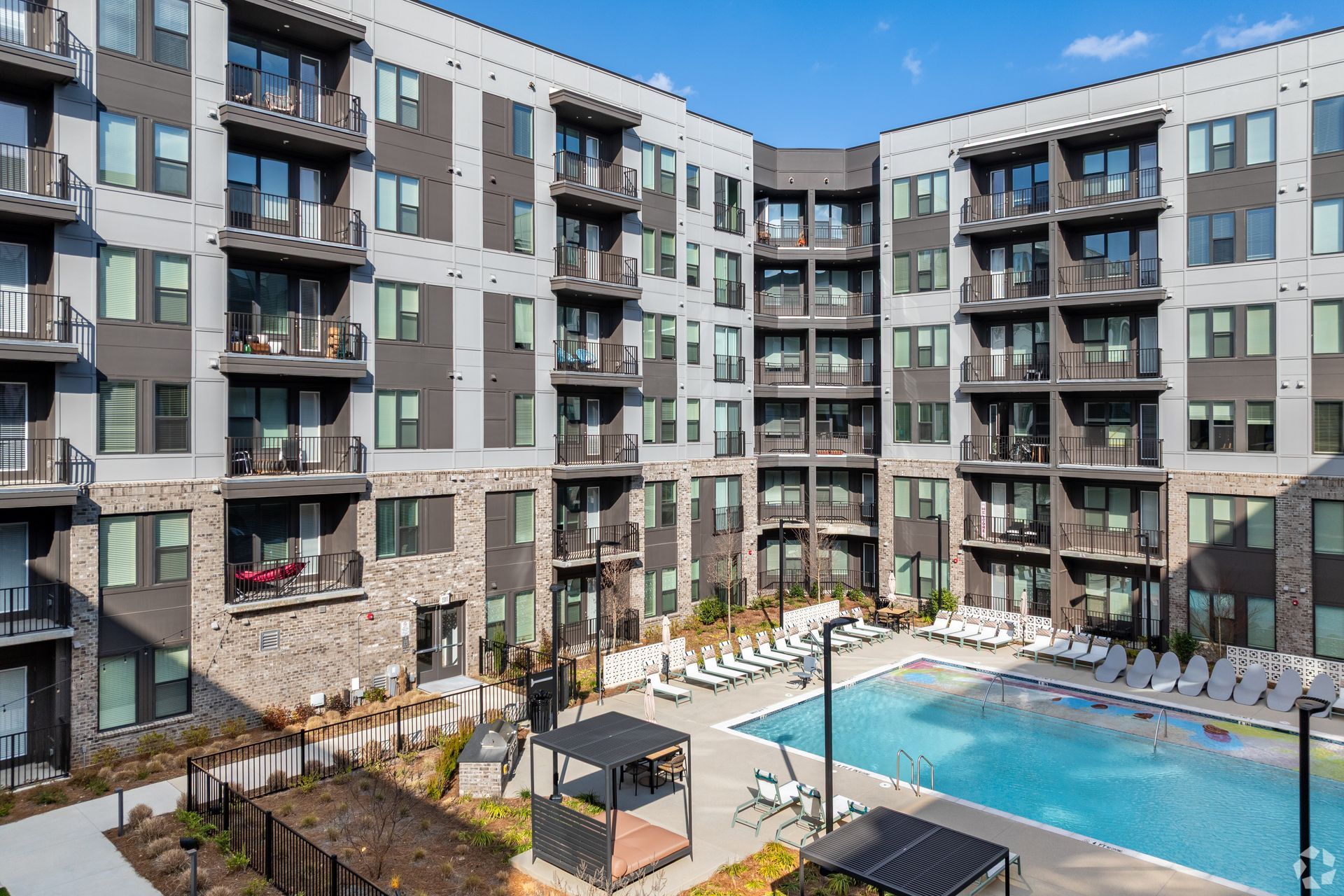 An apartment complex featuring a courtyard swimming pool, patio furniture, and stone and grey exterior walls.