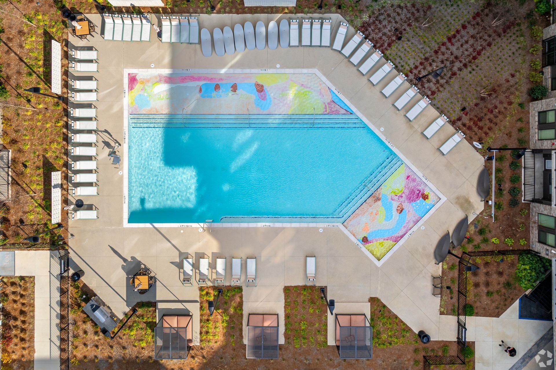 Aerial view of a swimming pool with lounge chairs, cabanas, and colorful decorative patterns on the pool deck.