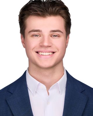 Studio headshot of a smiling person in a blue blazer and white shirt against a white background