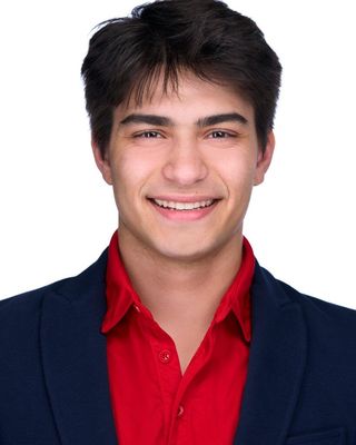 Smiling person in a red shirt and dark blazer against a white background