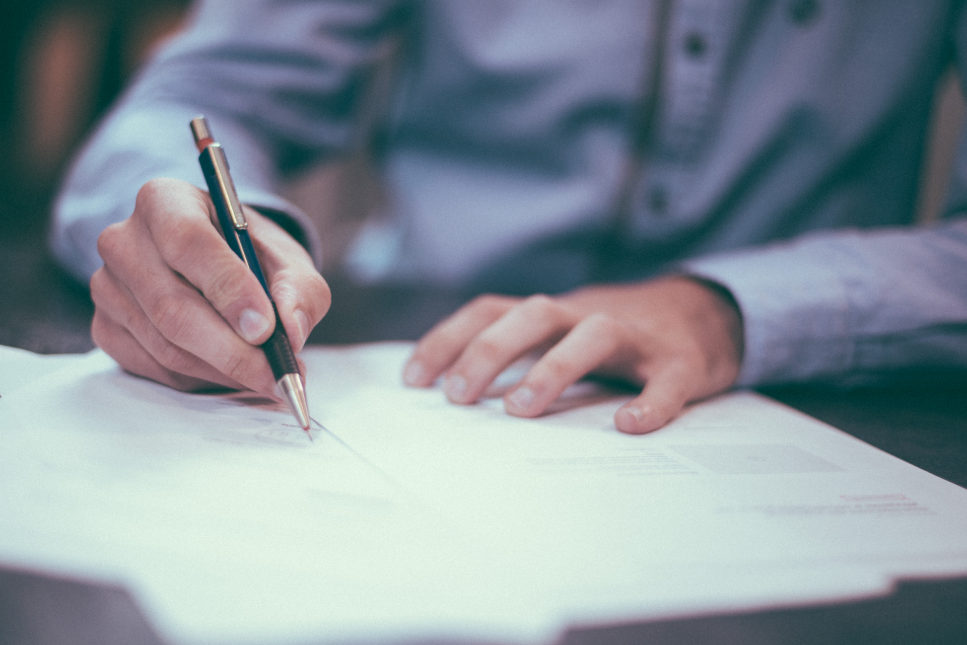 Hand writing on white paper with a pen at a desk