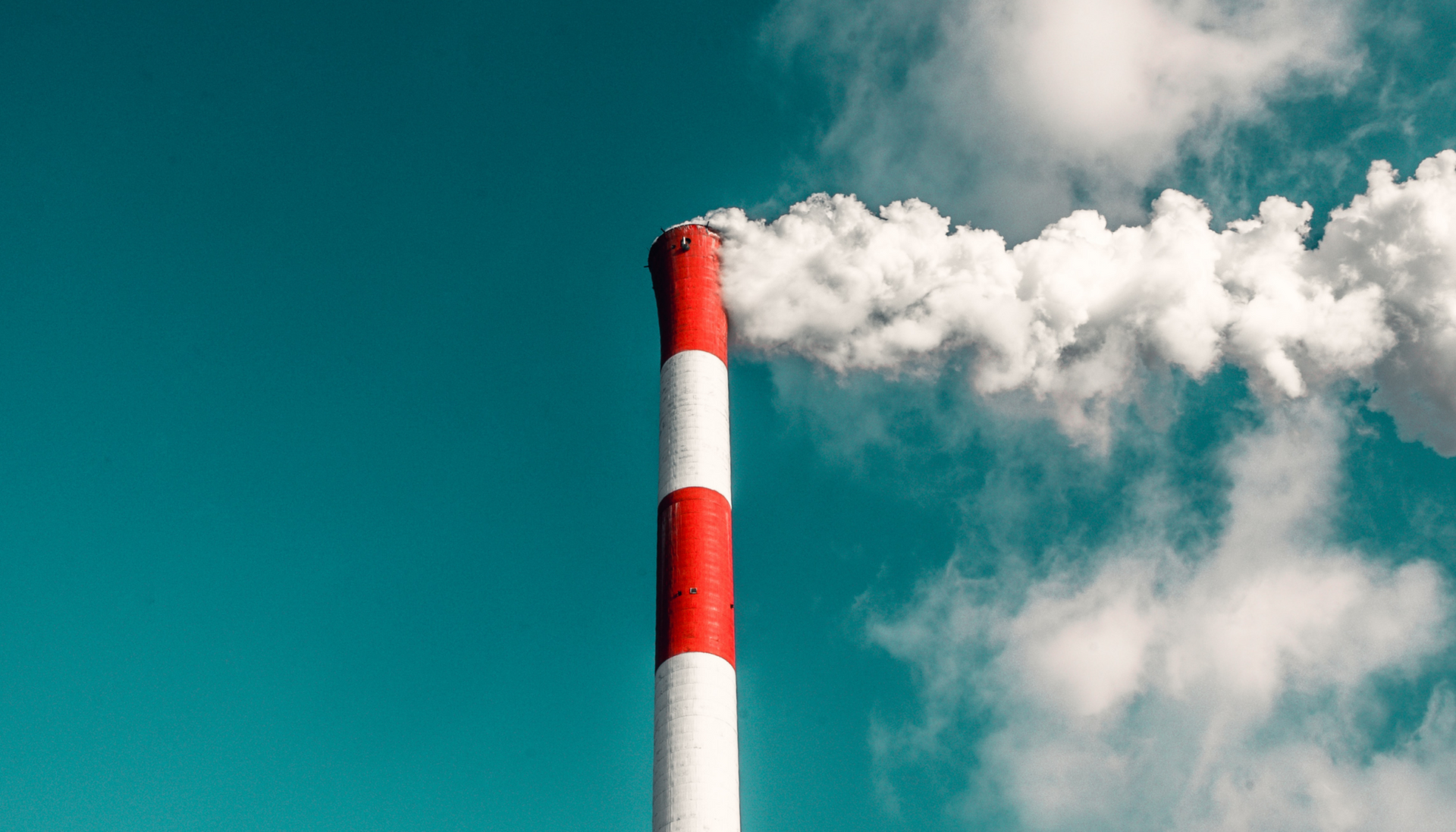 Red-and-white smokestack releasing white smoke against a blue sky