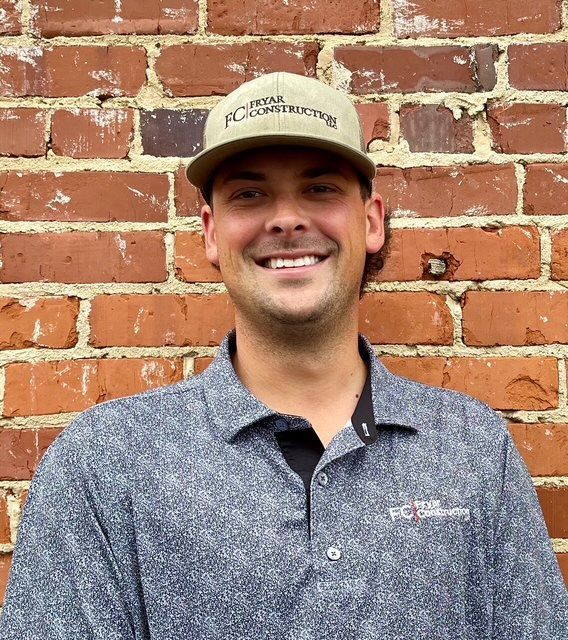 Man with a beard in a black shirt, smiling in front of a green wall.