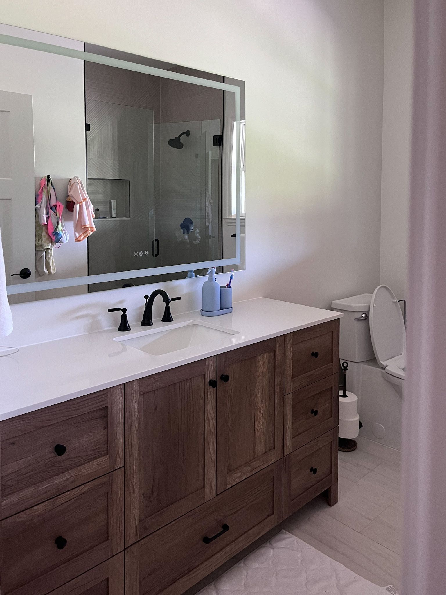 Bathroom vanity with large mirror, dark wood cabinets, and black faucet on a white countertop.