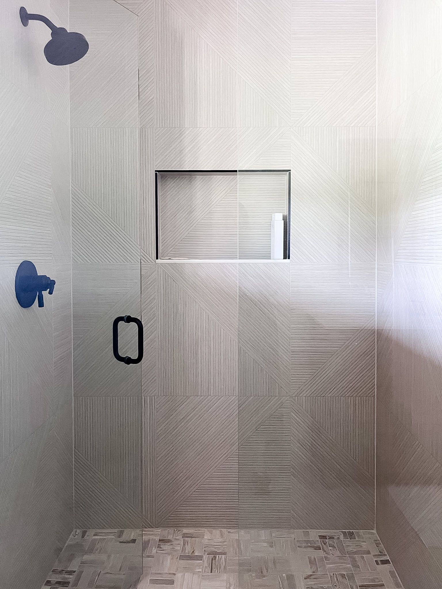 Small tiled shower with two blue fixtures, a black handle, and a rectangular niche in the wall.