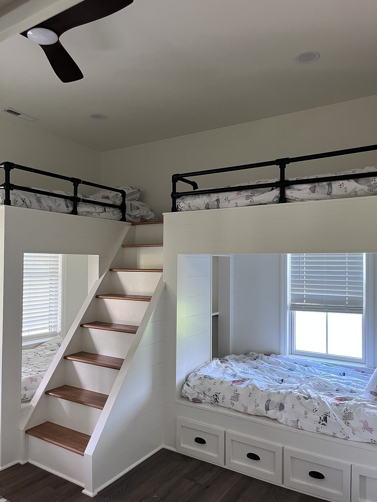 Kids’ bedroom with loft bed, stairs, and a window seat with drawers and patterned bedding