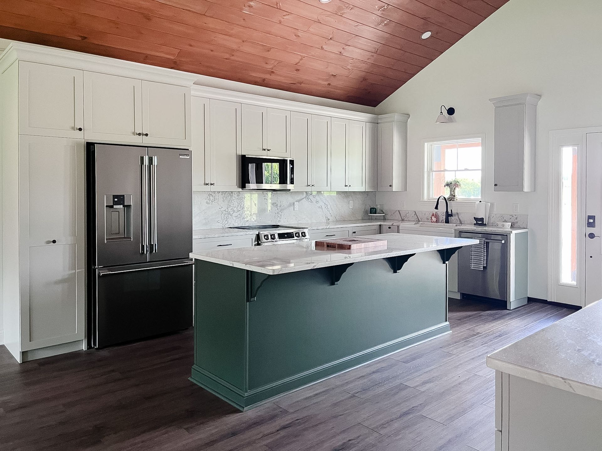 Modern kitchen with white cabinets, dark wood ceiling, black fridge, and a green island