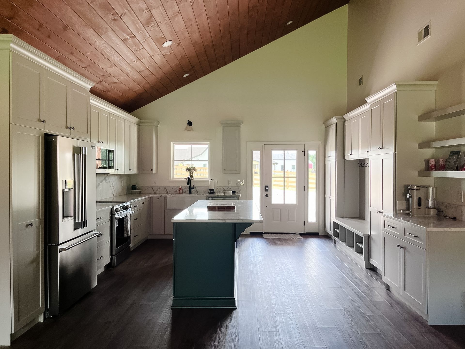 Bright kitchen with vaulted wood ceiling, white cabinets, stainless fridge, and a central island.