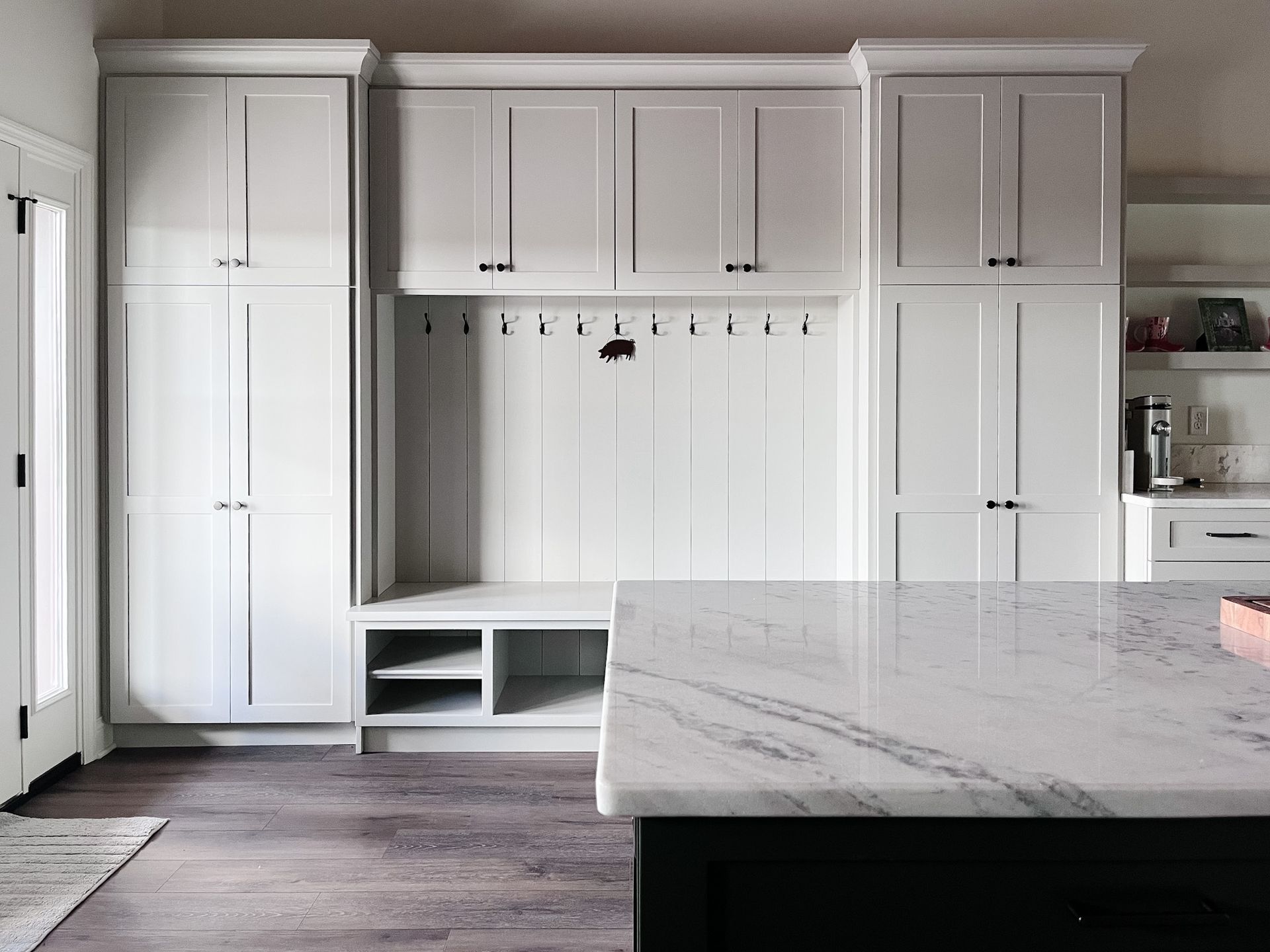 Bright white built-in cabinets and bench in a modern mudroom with marble island in foreground