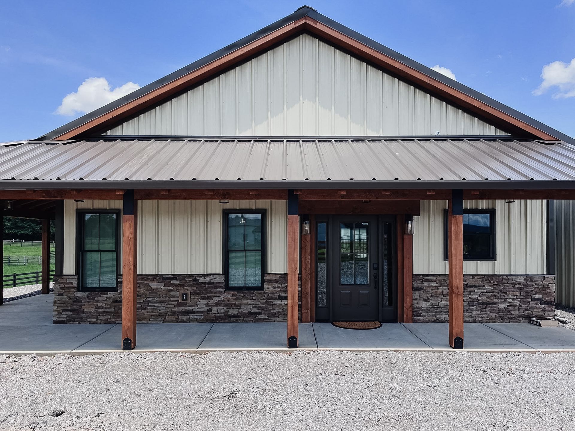 Front view of a modern house with a metal roof, stone base, and covered porch