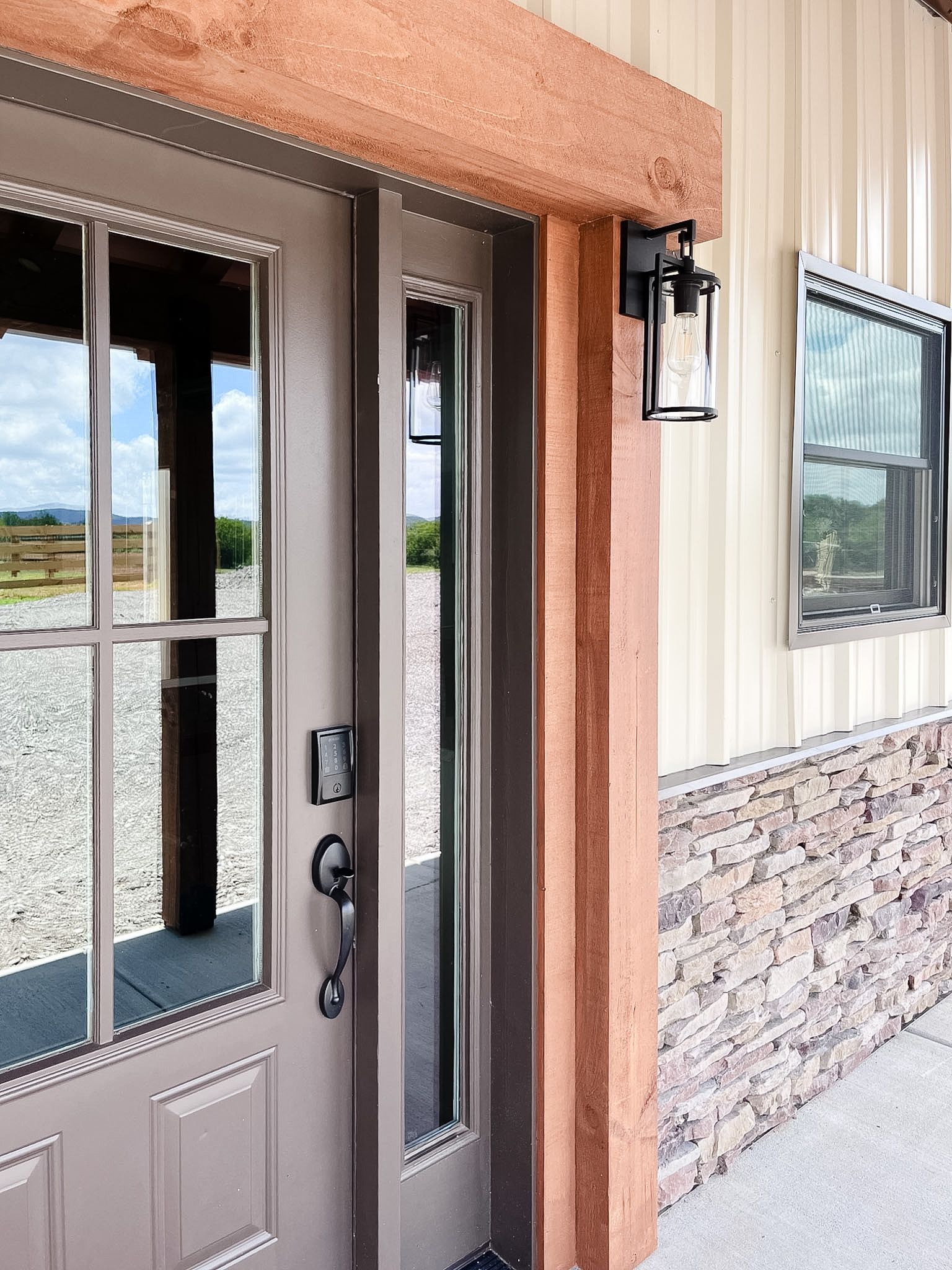 Front entrance with a glass-paneled door, stucco walls, and stone siding beside a window.