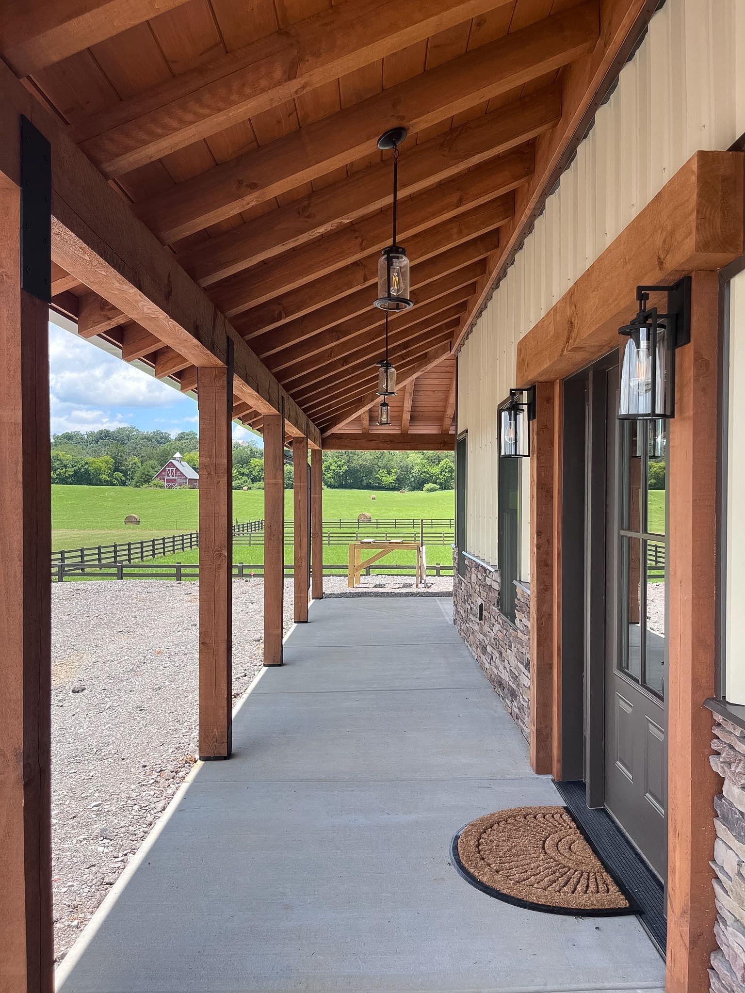 Covered porch with wooden beams, concrete floor, and countryside view beyond the railing.