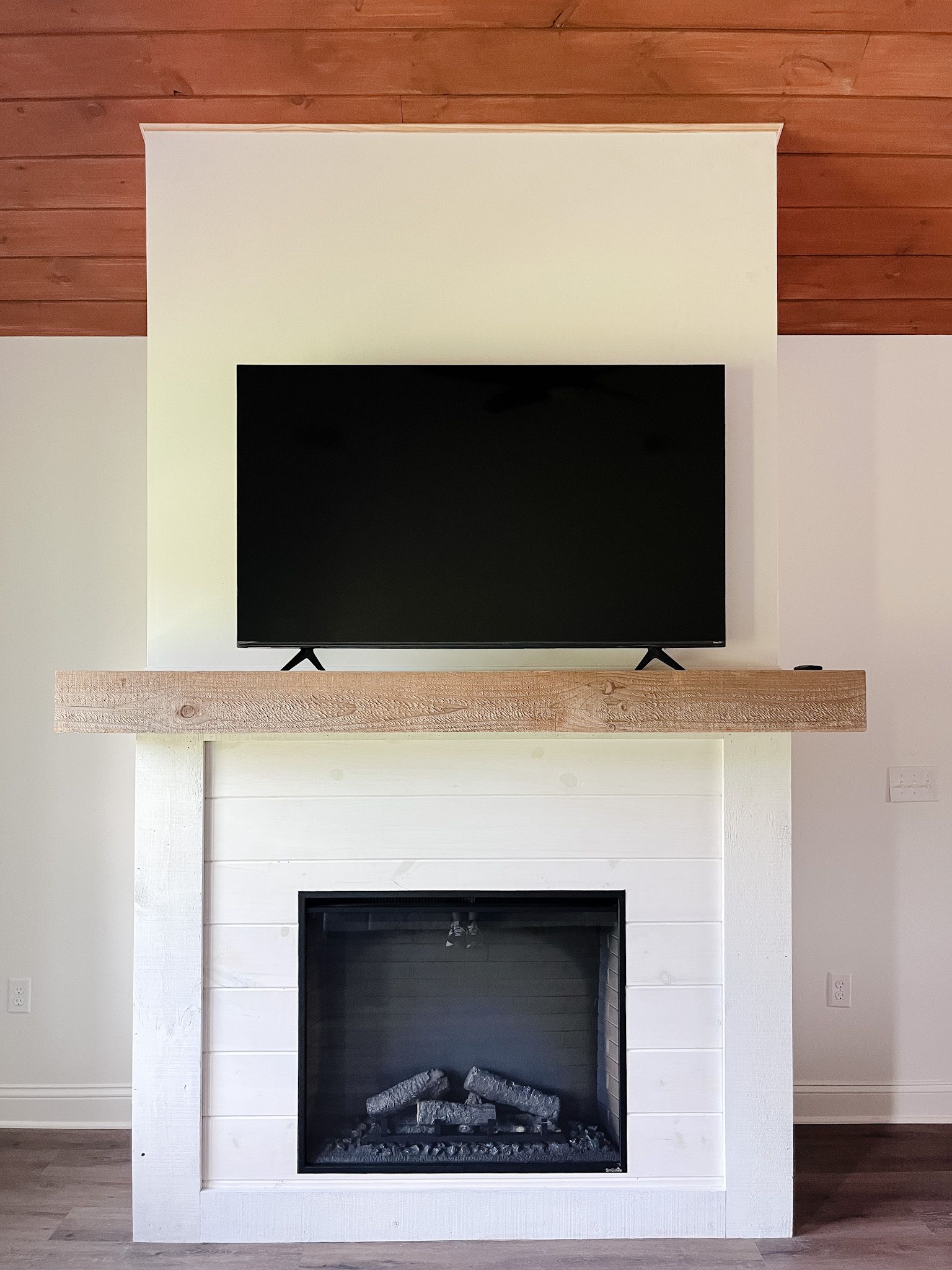 Modern fireplace with white surround, wood mantel, and a flat-screen TV above.