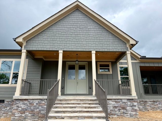 Front entrance of a gray house with stone steps, white trim, and a covered porch.