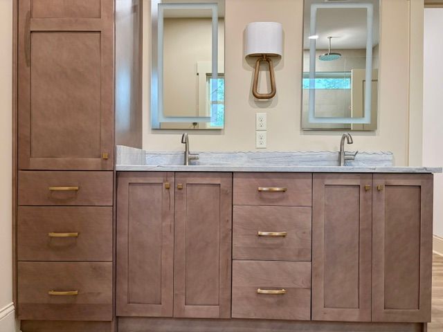 Modern bathroom vanity with wood cabinets, marble countertop, sink, and two mirrors under a wall sconce.