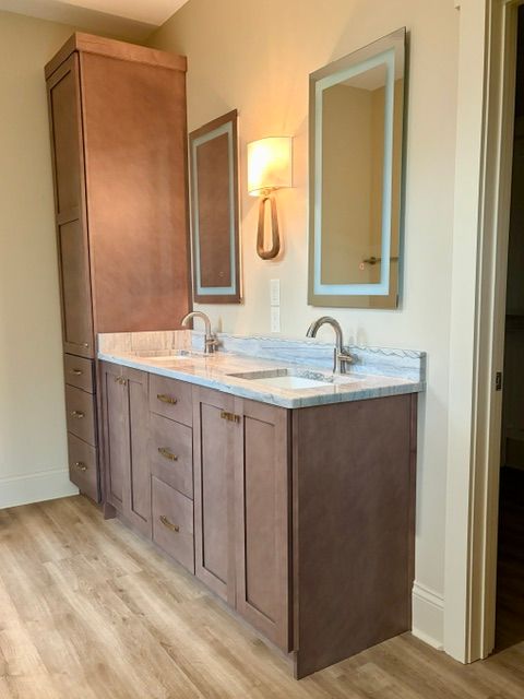 Wood vanity with marble countertop and double sinks, flanked by mirrors in a bathroom