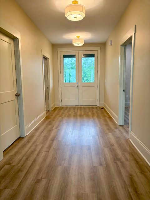 Bright hallway with wood flooring, white doors, and two ceiling lights leading to a glass door.