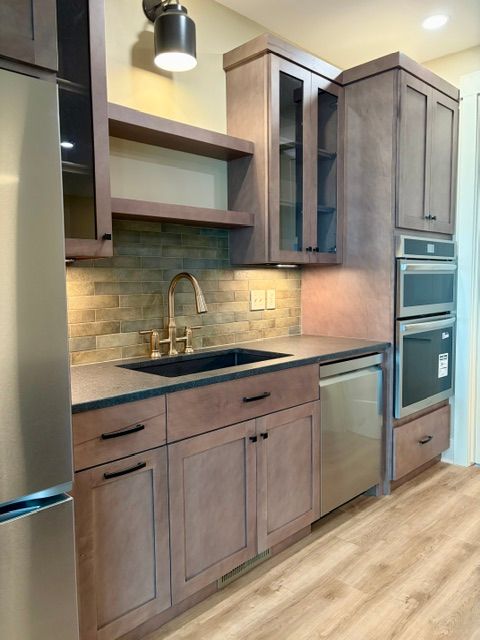 Modern kitchen with wood cabinets, stainless appliances, black countertop, and tiled backsplash