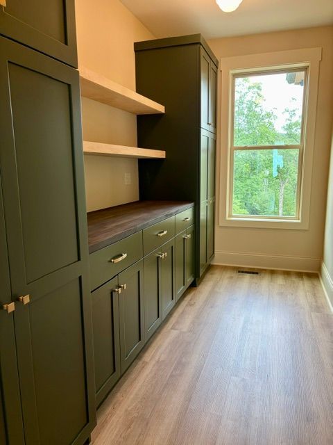 Built-in olive cabinets and shelves in a bright, narrow closet or pantry with a window at the end.