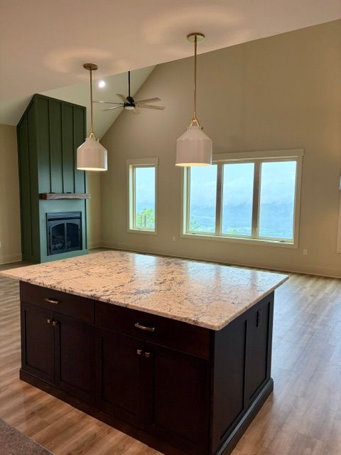 Modern kitchen with dark island, pendant lights, fireplace, and large windows overlooking water