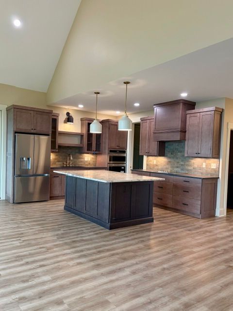 Spacious modern kitchen with dark wood cabinets, island, stainless fridge, and light wood flooring.