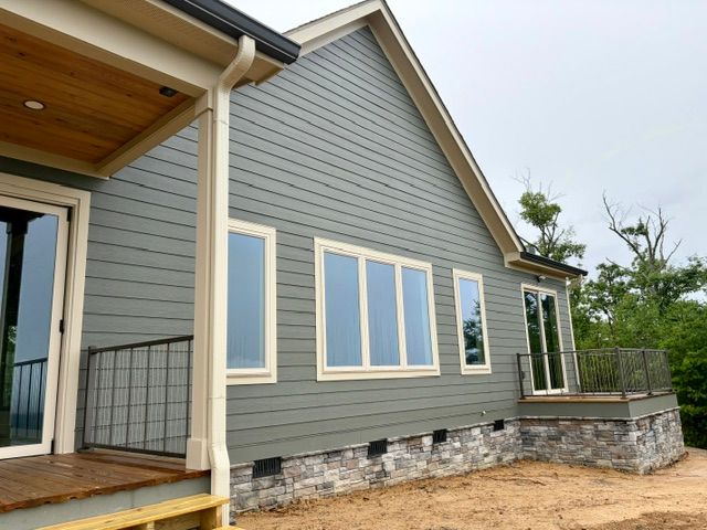 Modern house exterior with gray siding, large windows, and a stone foundation