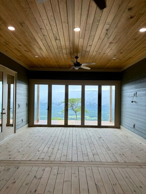 Empty sunroom with wood plank ceiling, floor, and wall, facing large glass doors with mountain views.