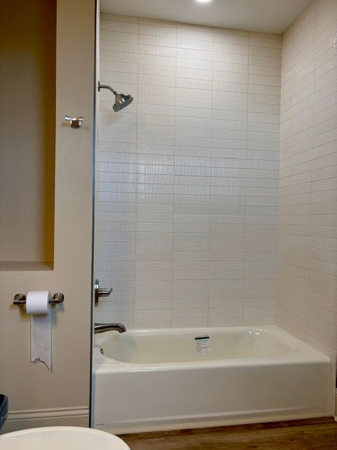 Bathroom with a white bathtub, tiled shower wall, and toilet paper holder on the left wall