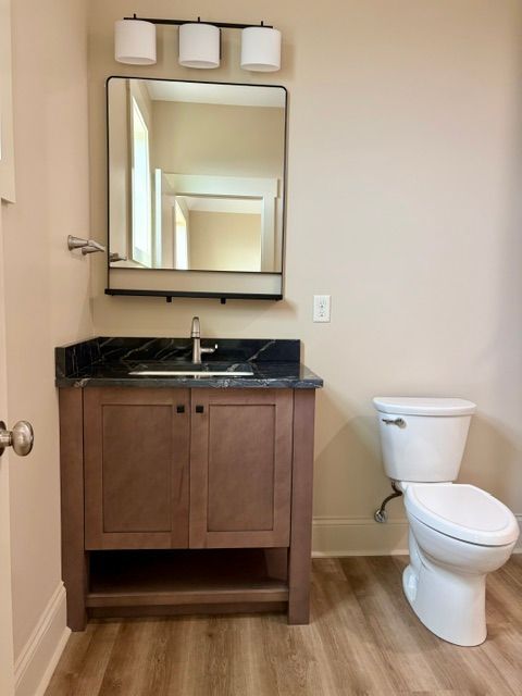 Small bathroom with wood vanity, mirror, three lights, black countertop, and white toilet.