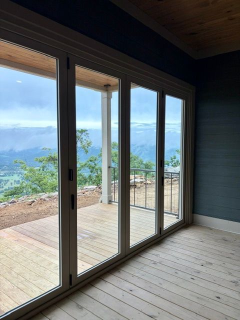 Sliding glass doors open to a wooden deck with mountain and sky views.