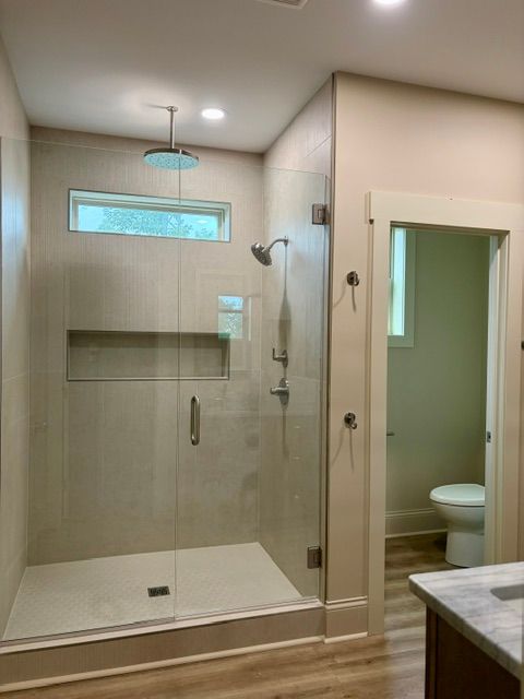 Glass walk-in shower with tiled walls, built-in shelf, and partial view of a bathroom vanity and toilet.